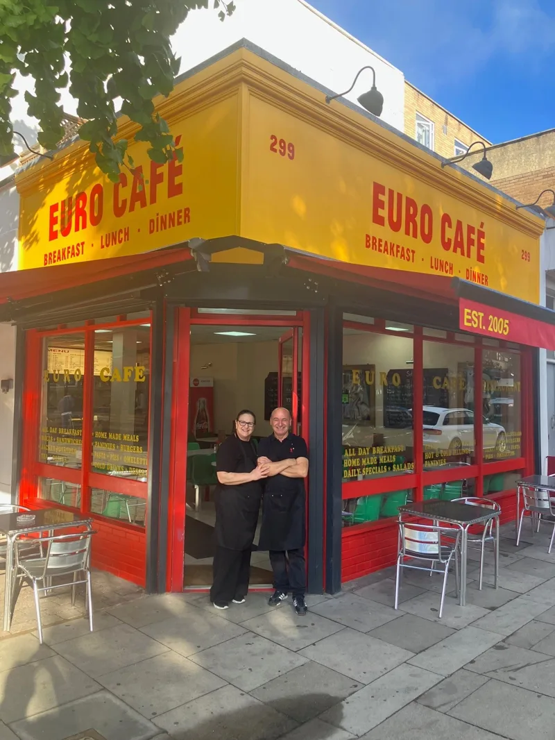Two people standing outside Euro Café on Caledonian Road under its new red and yellow sign