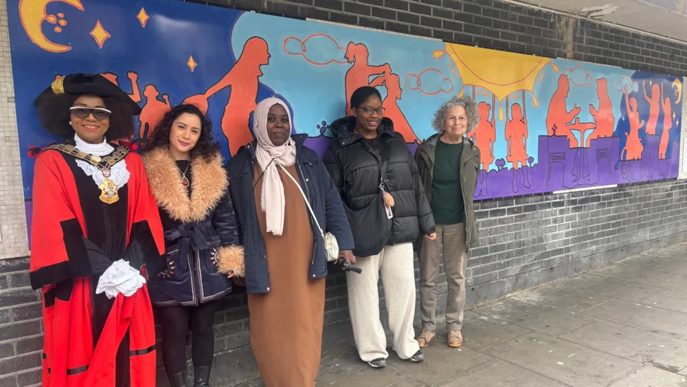 The Mayor of Islington, in mayoral robes, stands with the artist and three residents in front of an orange and purple mural on Wells Terrace