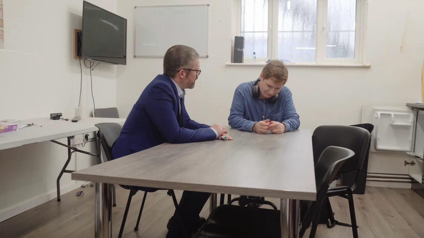 The supply teacher and an autistic student at a classroom table, in a scene from The Supply Teacher